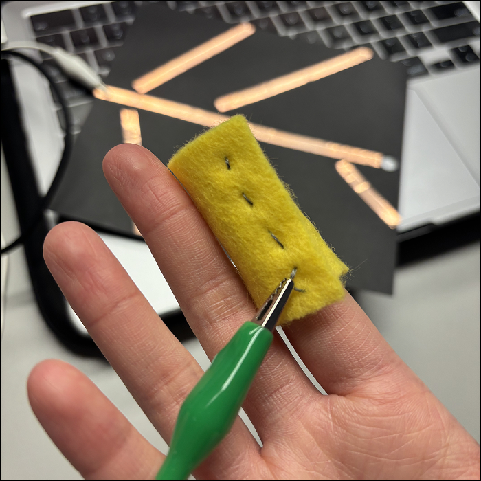 I sewed a small piece of fabric with conductive fabric, and attach one alligator clip on the thread.
